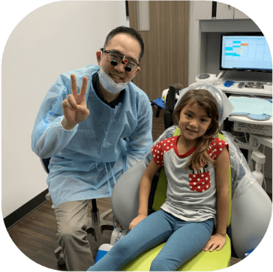 Pecan Grove Texas dentist smiling and giving peace sign with little kid in dental chair
