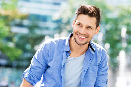 Young man in light blue shirt smiling outdoors