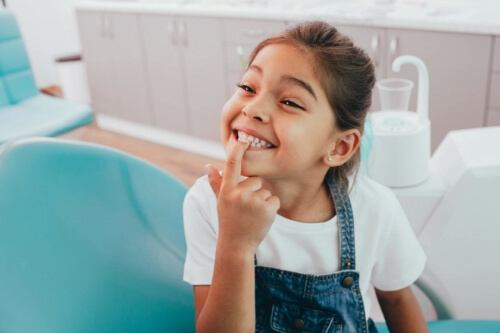 Young girl in dental chair pointing to her smile