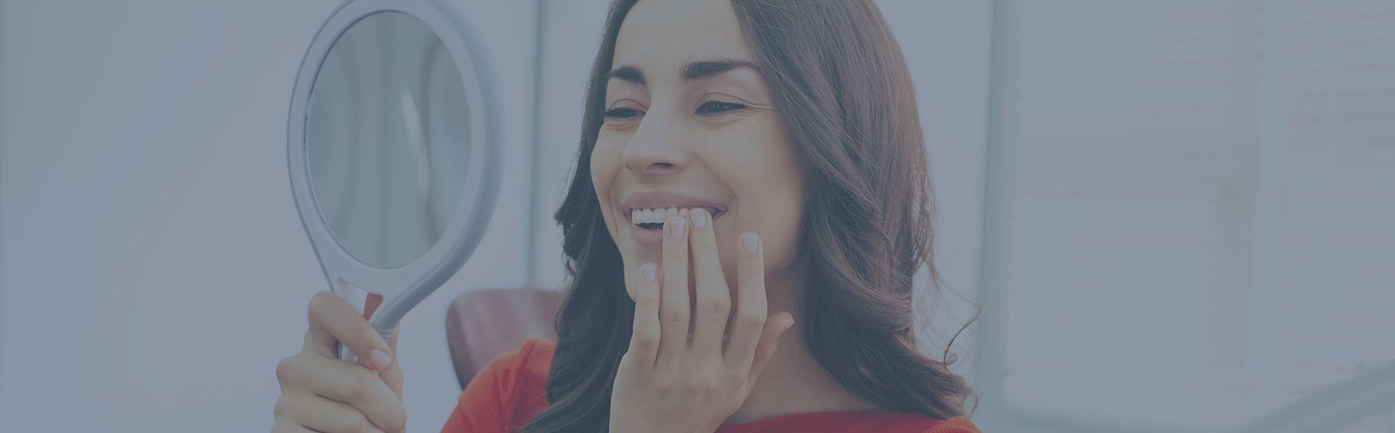 Woman admiring her smile in a mirror after cosmetic dentistry treatment in Pecan Grove