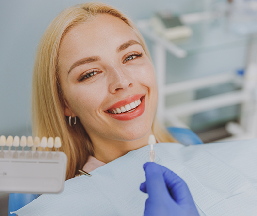 Dental holding a veneer in front of a patient's smile