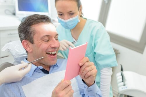 Dental patient looking at his smile in mirror with dental crowns in Pecan Grove