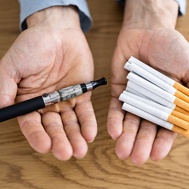Person holding a vape and several cigarettes