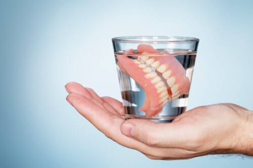 Hand holding a glass of water with dentures soaking in it