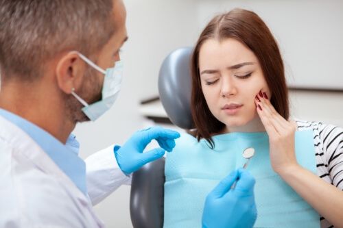 Woman holding her cheek in pain while visiting emergency dentist in Pecan Grove