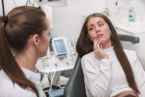 Woman holding her cheek in pain while talking to emergency dentist