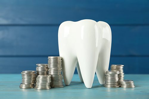 A large ceramic tooth model surrounded by silver coins