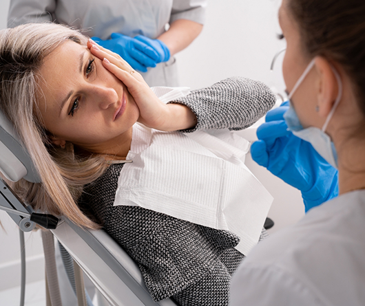 Woman holding her cheek in pain while talking to her emergency dentist