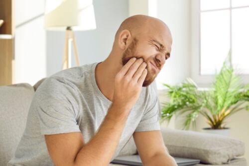 Man sitting on couch and holding his jaw in pain