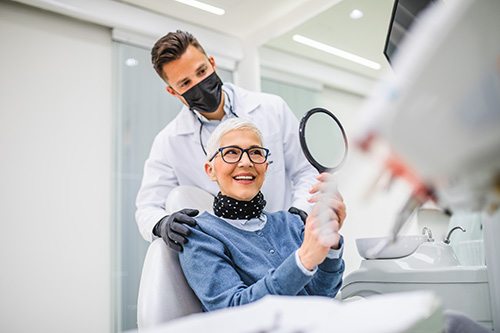 Woman in dental chair smiling at reflection with dentist looking over her shoulder