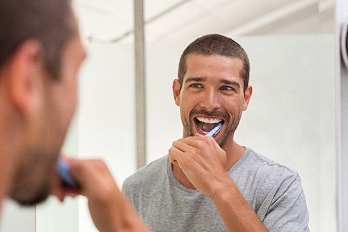 Man in gray shirt brushing teeth at mirror