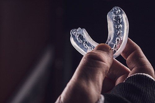 Fingers holding clear mouthguard with dark background