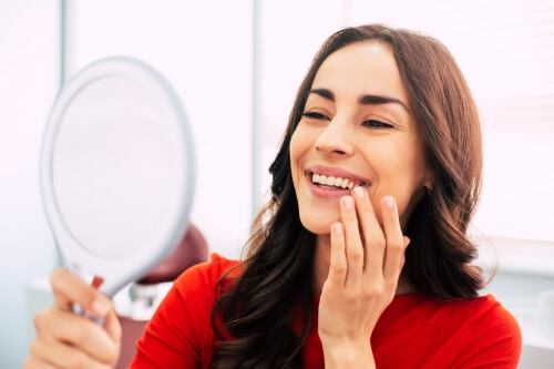 Young woman in dental chair admiring her smile in mirror