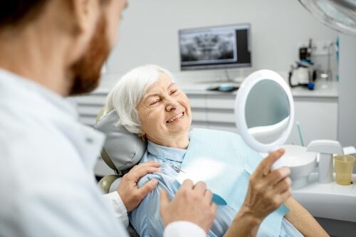 Senior woman in dental chair looking at her smile in mirror