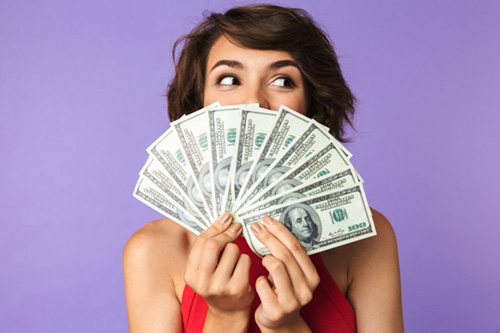 Woman holding a fan of paper money in front of her face