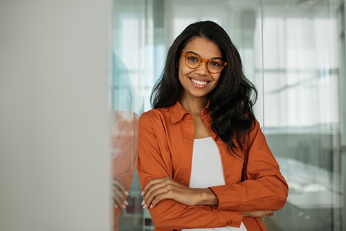Woman with orange jacket and glasses smiling with arms folded