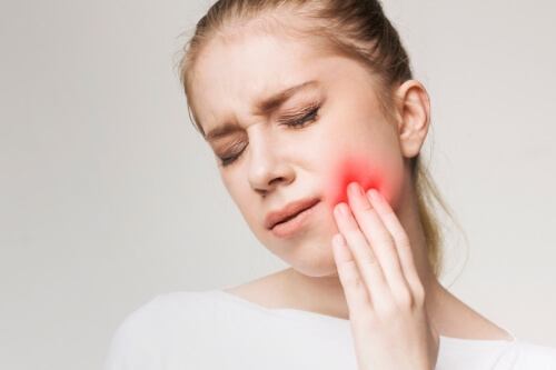 Wincing woman holding her cheek in pain with her cheek highlighted red