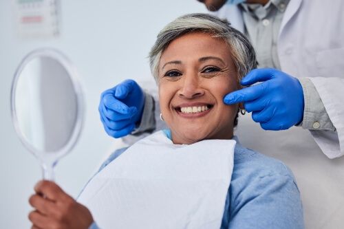 Woman holding mirror and smiling in dental chair
