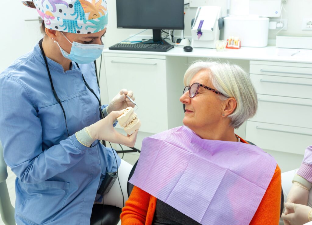 Dentist showing model teeth to patient in orange sweater