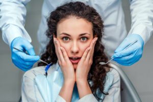 Patient in dentist’s chair holding hands to face in fear.